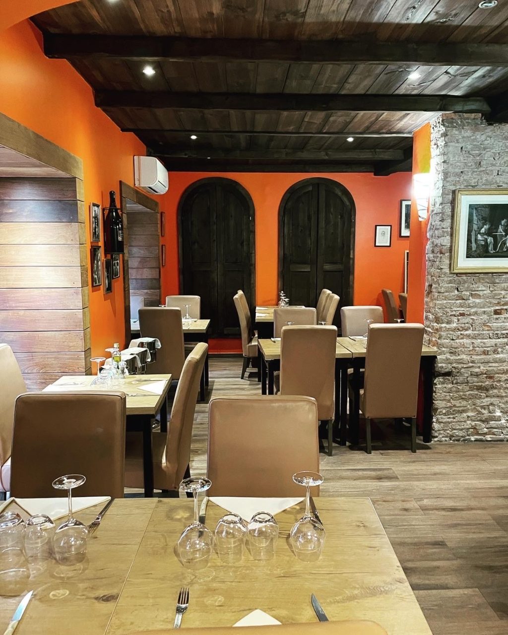 Salle intérieure de L'Auberge Ajaccienne à Ajaccio : murs orange, poutres en bois et pierres apparentes, tables dressées