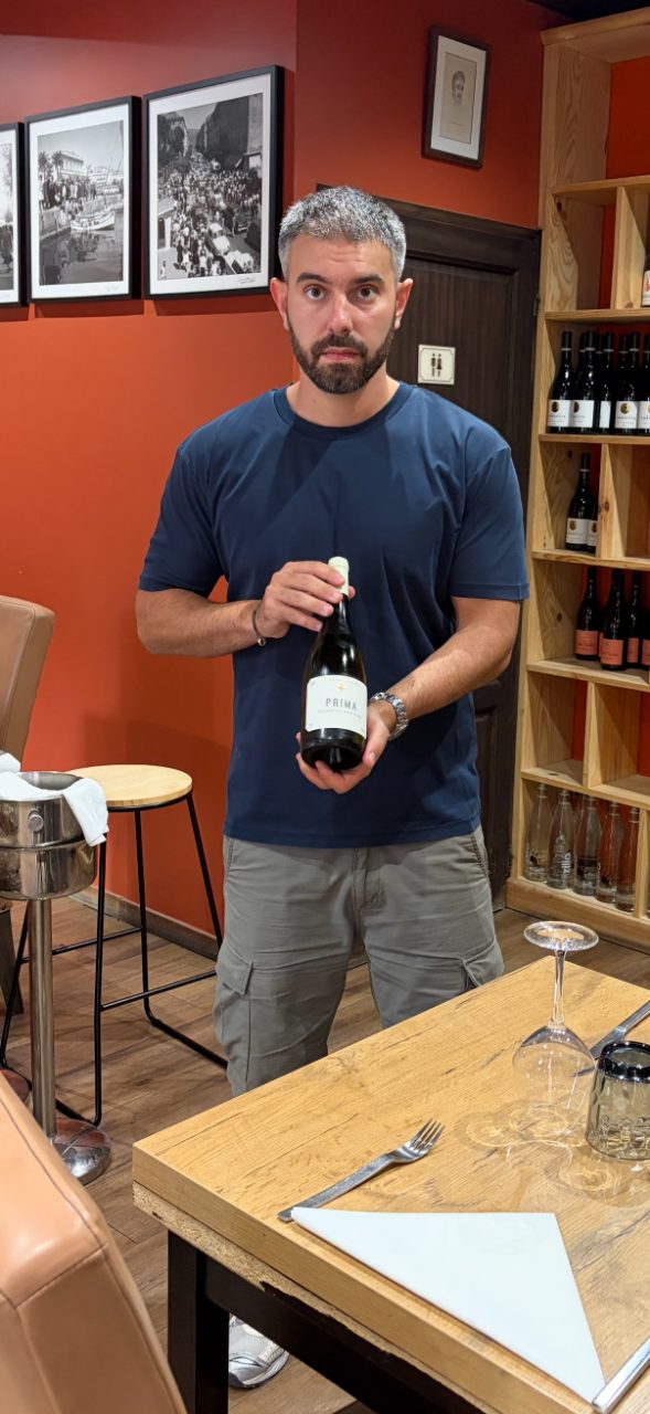 Simon présentant une bouteille de vin corse devant la cave à vins du restaurant